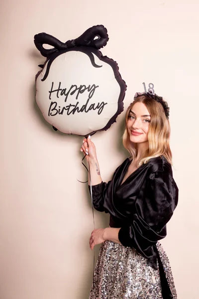 Woman holding a 'Happy Birthday' balloon with a bow on a plain background