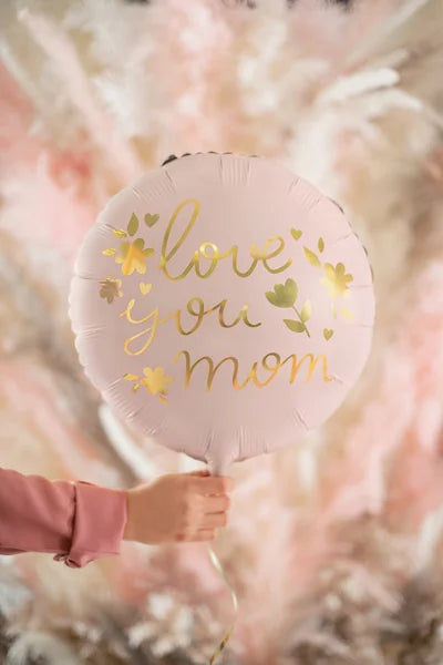 Pink balloon with 'love you mom' text held by a hand against a soft, blurred background