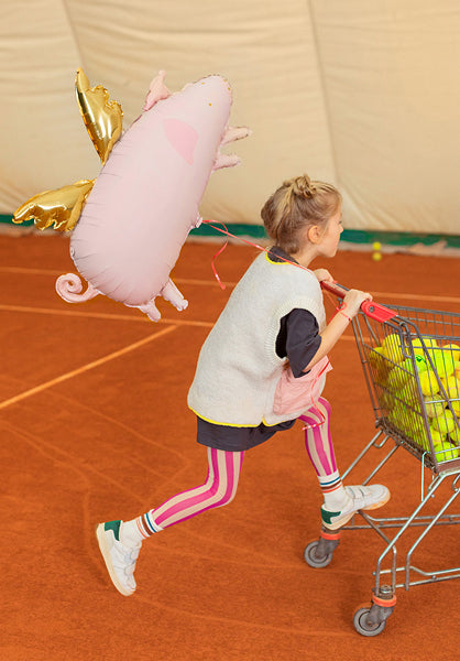 Child playing with a large inflatable pig toy on an indoor basketball court.